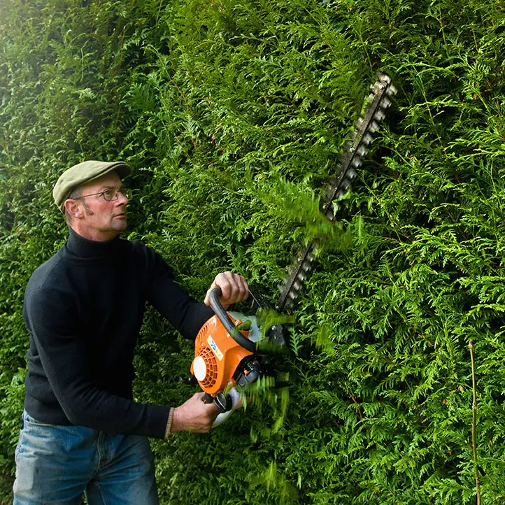 man trimming large hedges with hedge trimmer